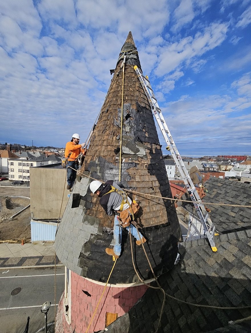 Roofers with hard hats and harnesses removing an old turret roof in Massachusetts